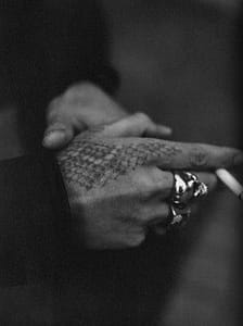 man's hand holding cigarette, tattooed with diamond rattler snakeskin pattern