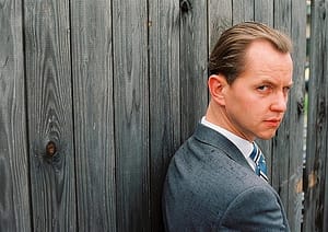 swing singer Max Raabe in suit, next to fence